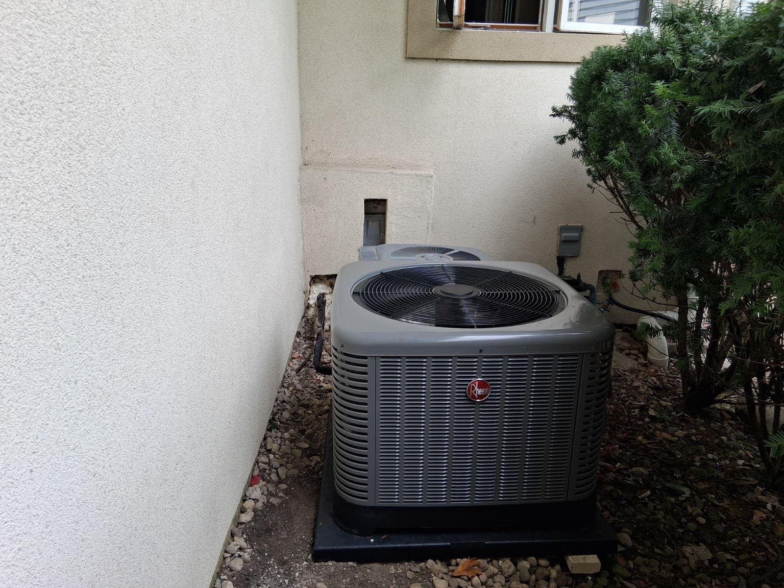 Rheem air conditioning condenser installed on a level pad in a narrow side yard
