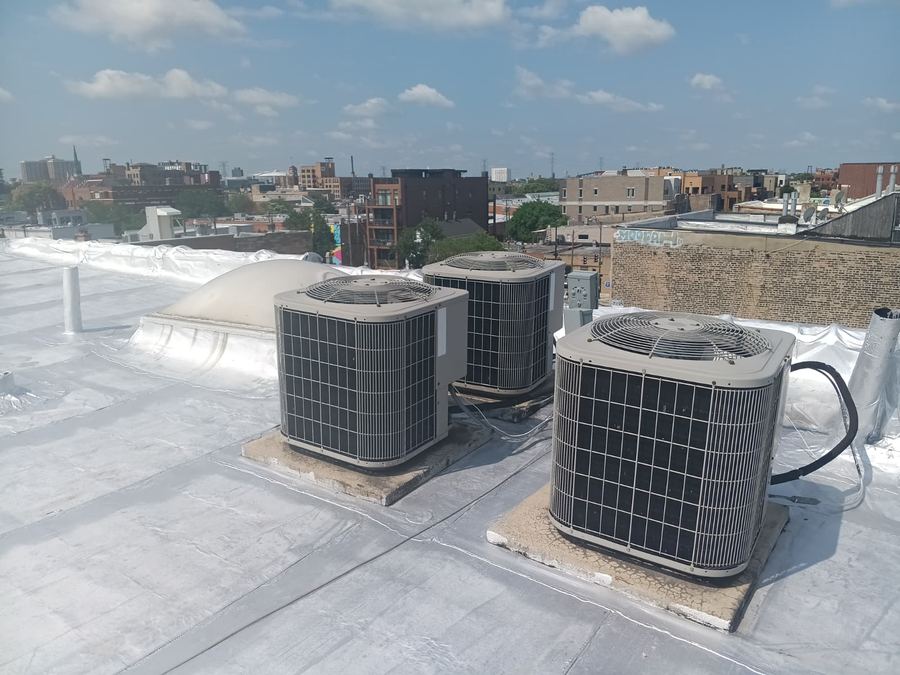 Three air conditioning condensers installed on a flat Chicago rooftop with the city skyline behind