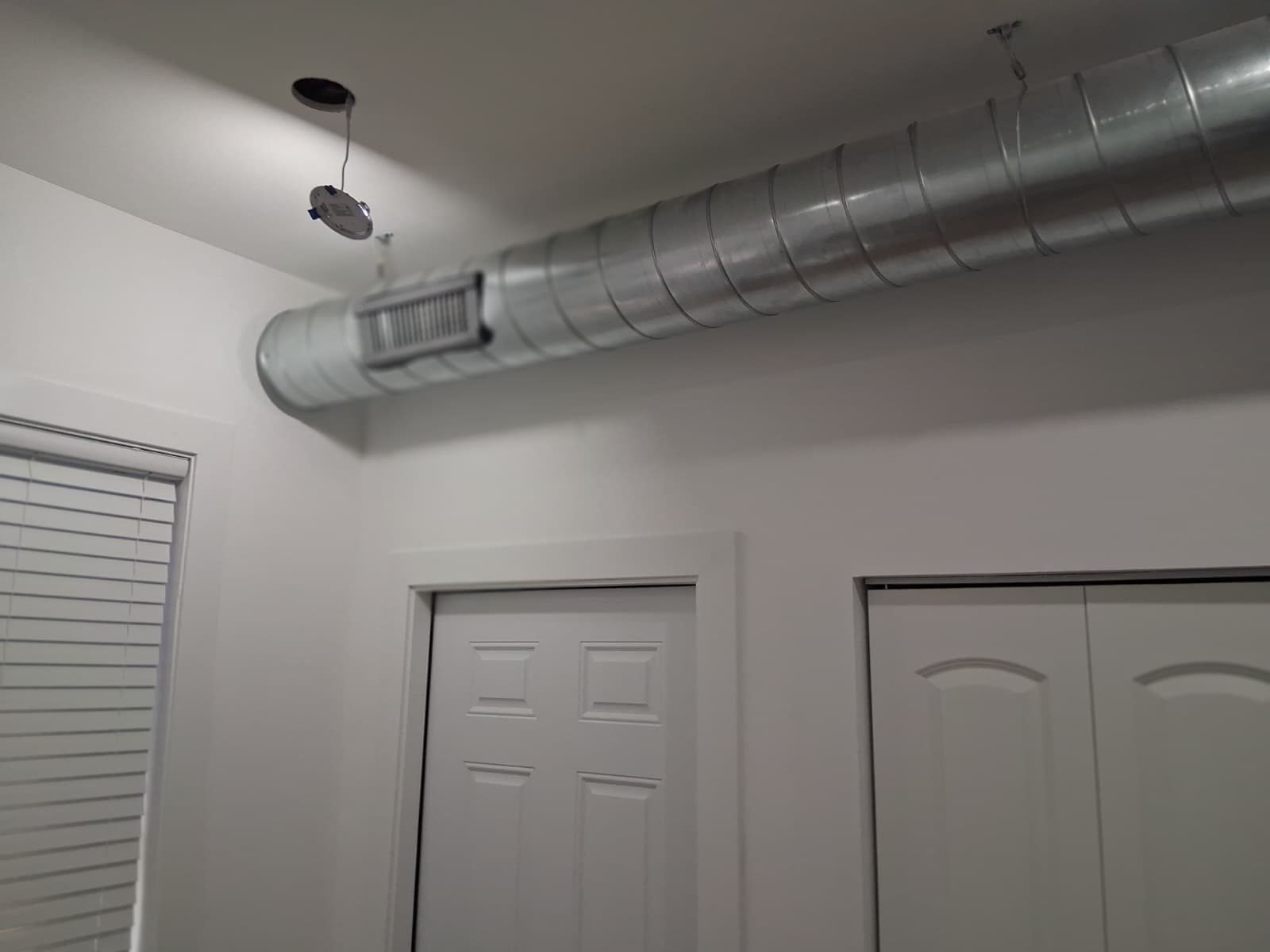 Round spiral supply duct with a grille running across a finished ceiling